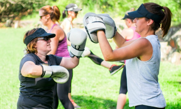 A healthy older woman practices boxing in the park on a sunny day